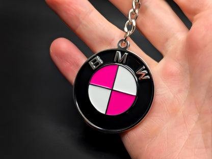 Hand holding a circular pink BMW enamel badge keychain to demonstrate the premium metallic weight and detailed 3D design.