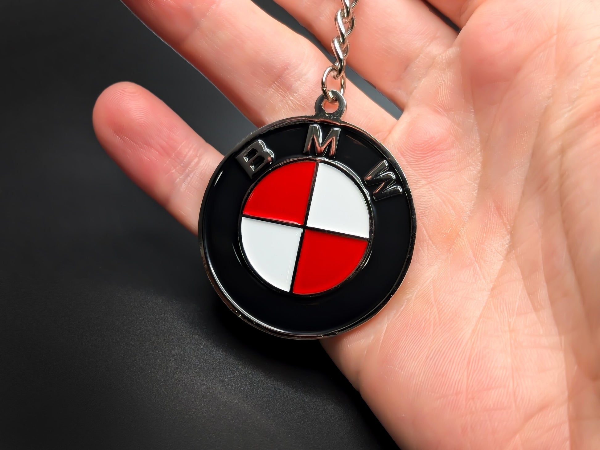 Hand holding a circular red and white BMW enamel badge keychain to demonstrate the premium metallic weight and 3D textures.