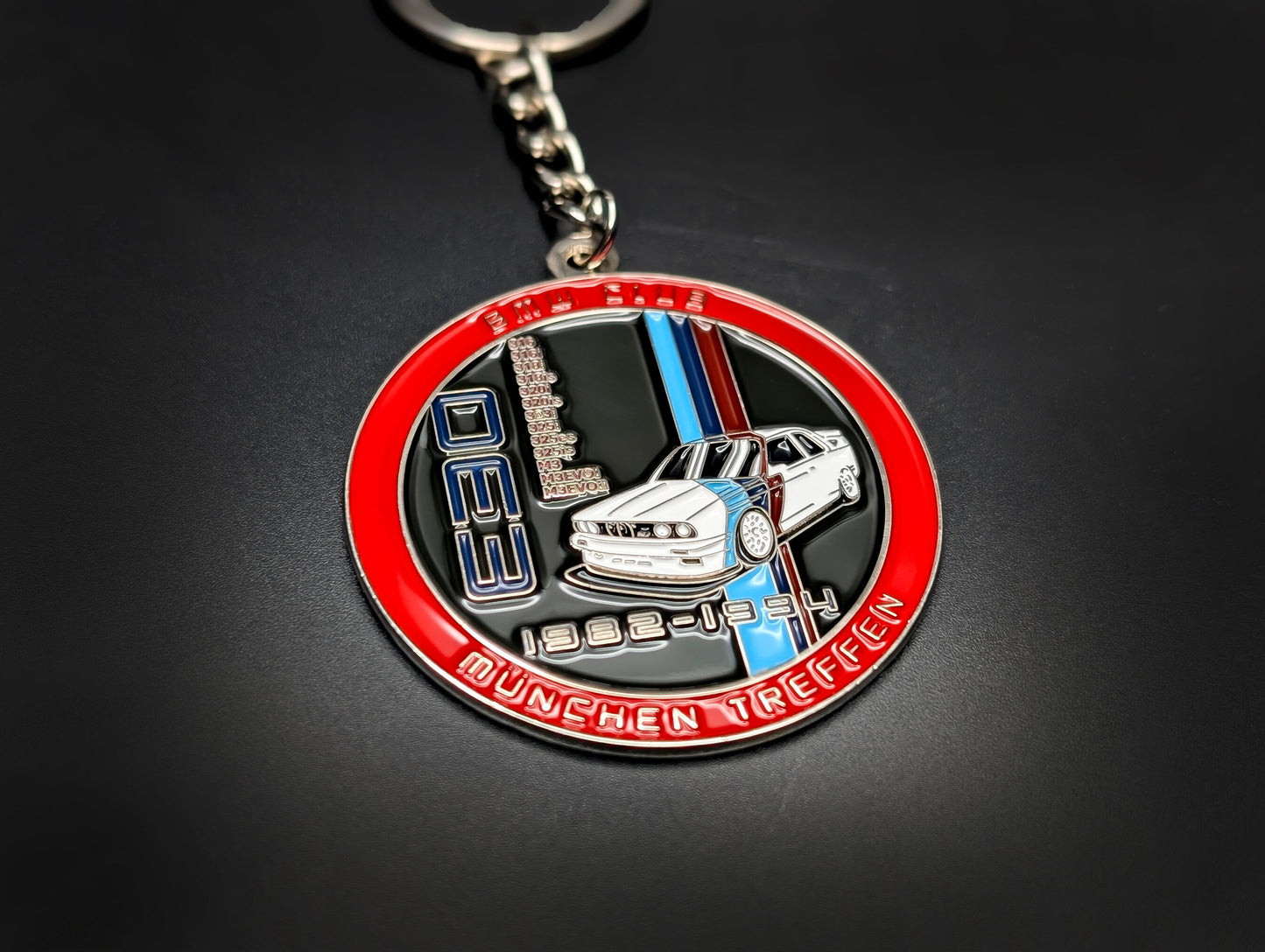 A hand holding the BMW E30 M3 badge keychain, showing the vibrant blue enamel and polished silver-tone metal.