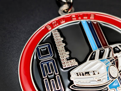 A BMW E30 M3 badge keychain with a silver chain and keyring, displayed on a sleek dark surface.