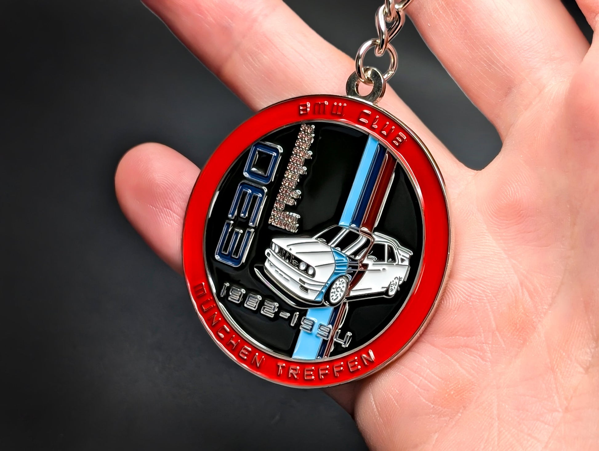Close-up of a circular metal badge keychain featuring a detailed BMW E30 M3 illustration and the M motorsport logo.