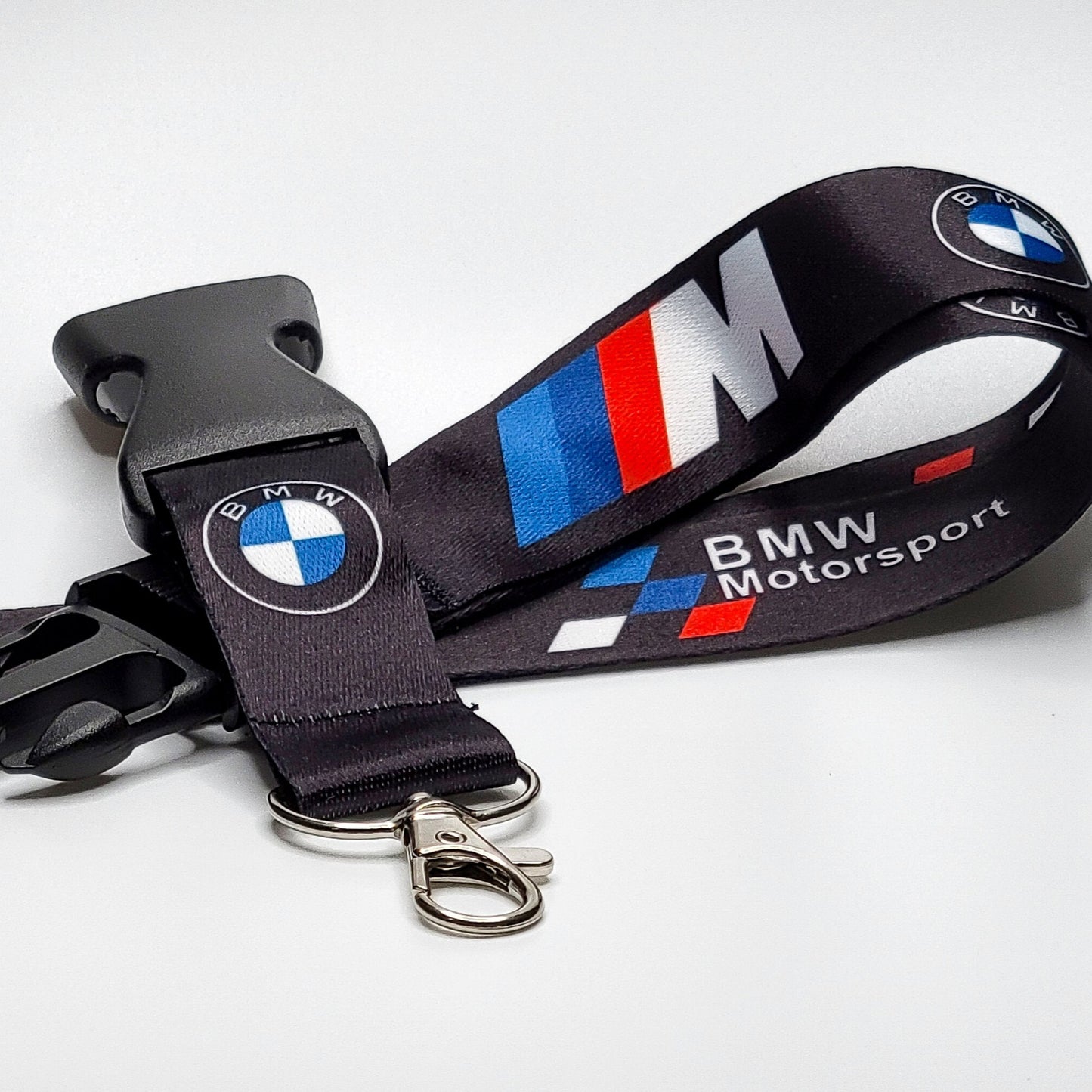 Black BMW Motorsport lanyard with an embroidered BMW roundel, an M logo in blue-red-white stripes, and BMW Motorsport text, coiled with a black breakaway clip and silver clasp on white.