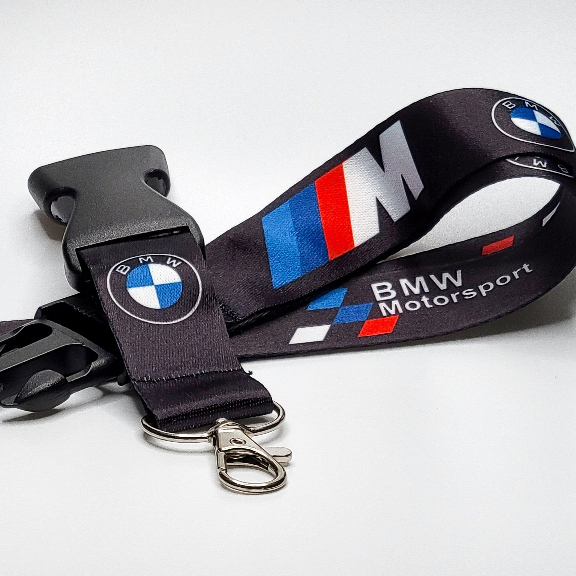 Black BMW Motorsport lanyard with an embroidered BMW roundel, an M logo in blue-red-white stripes, and BMW Motorsport text, coiled with a black breakaway clip and silver clasp on white.