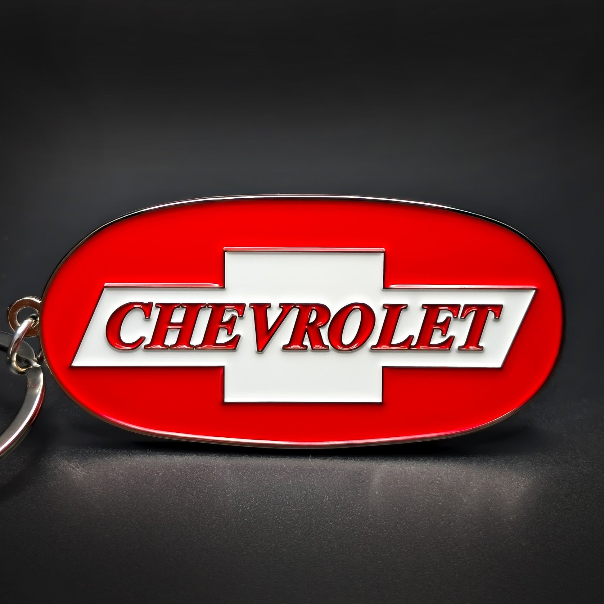 Double-sided metal Chevrolet badge keychain, oval chrome-edged red enamel medallion with a white bowtie and “CHEVROLET” lettering across the center, on a silver split ring.