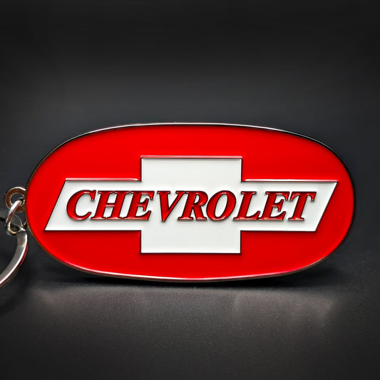 Double-sided metal Chevrolet badge keychain, oval chrome-edged red enamel medallion with a white bowtie and “CHEVROLET” lettering across the center, on a silver split ring.