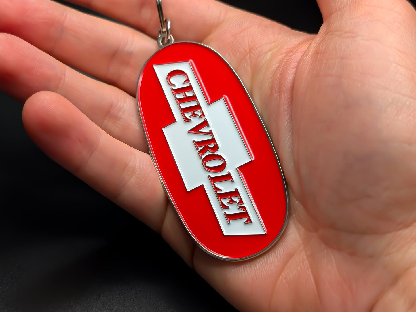 Hand holding an oval Chevy Trucks enamel badge keychain to demonstrate the premium metallic weight and vibrant 3D color finish.
