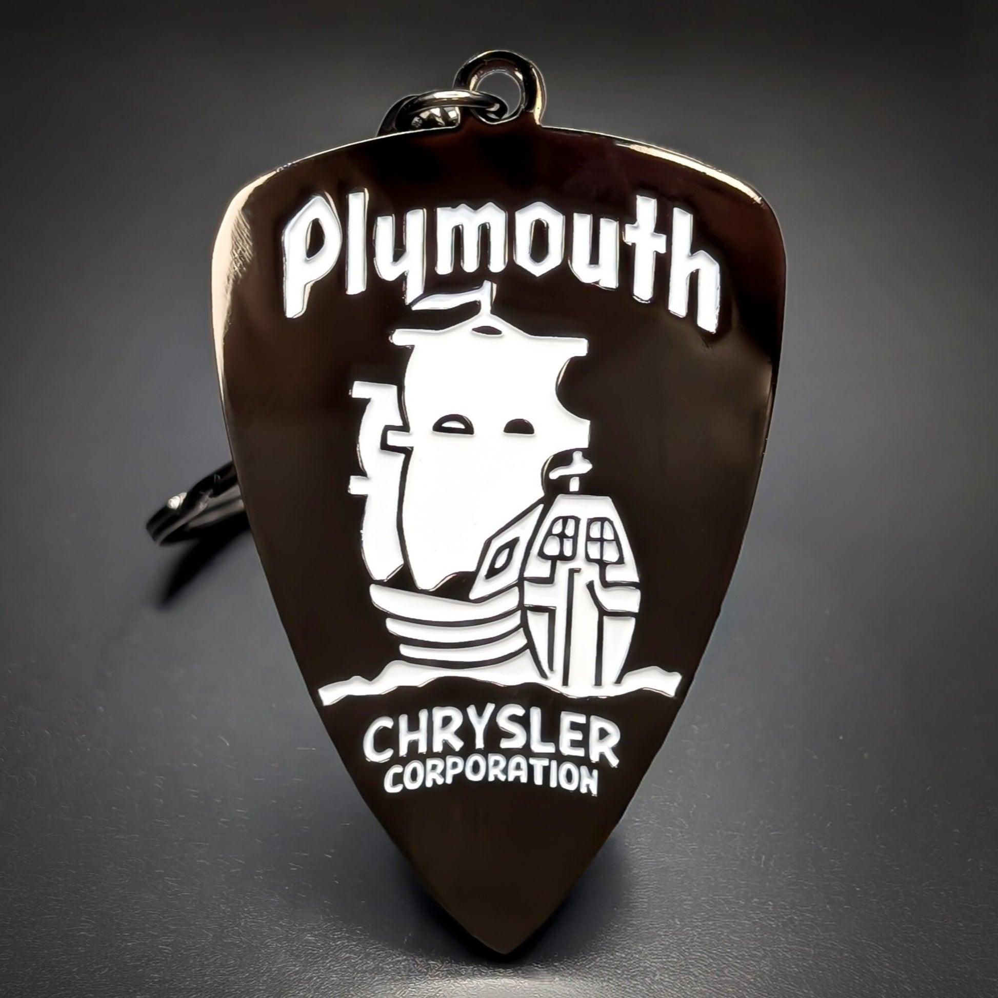 Double-sided metal Chrysler Plymouth badge keychain, a dark bronze shield with ‘Plymouth’ script above a white ship illustration and ‘CHRYSLER CORPORATION’ text, on a jump ring on a dark background.