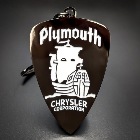 Double-sided metal Chrysler Plymouth badge keychain, a dark bronze shield with ‘Plymouth’ script above a white ship illustration and ‘CHRYSLER CORPORATION’ text, on a jump ring on a dark background.