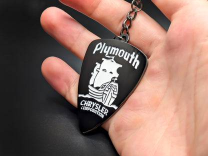 Hand holding a Plymouth Chrysler Corporation enamel badge keychain to demonstrate the size and premium metallic construction.