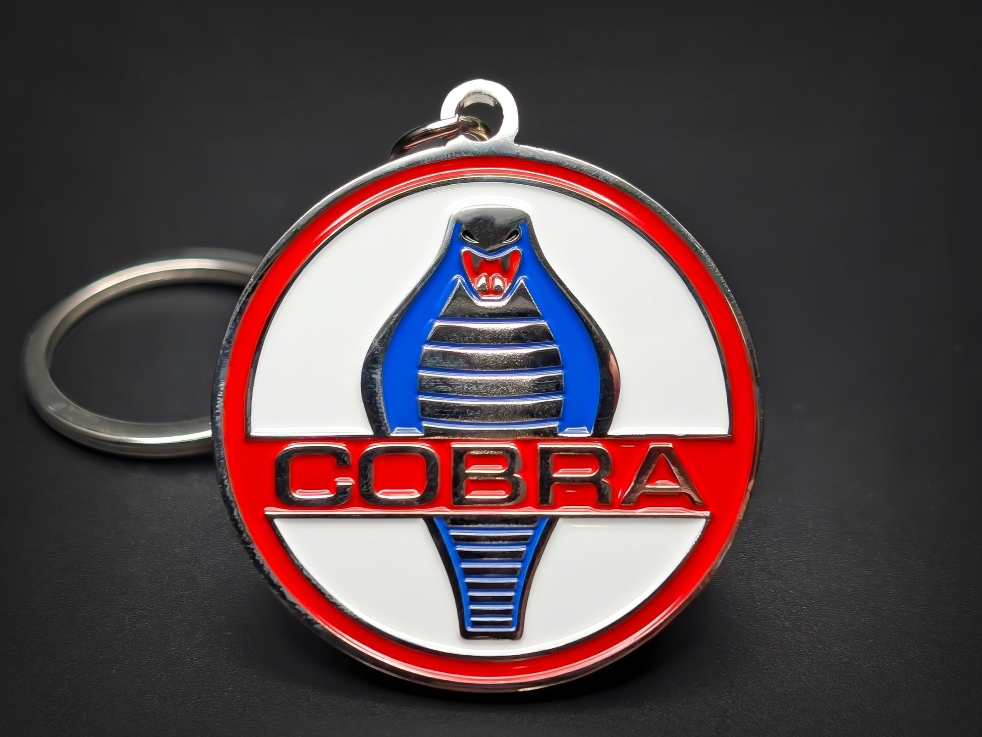 Shelby Cobra badge keychain with a blue and silver cobra logo on a white and red circular enamel base.