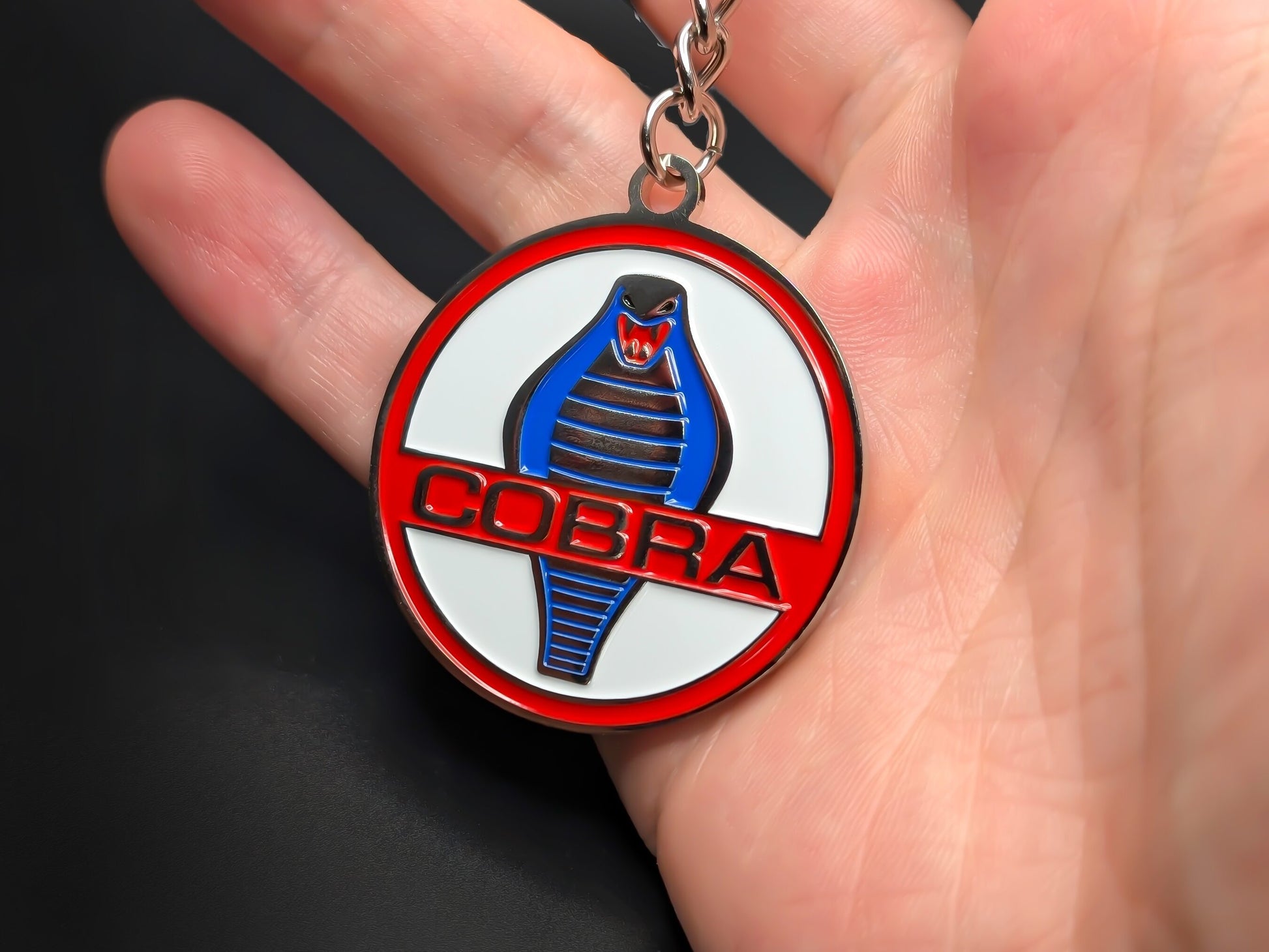 Hand holding a circular Shelby Cobra enamel badge keychain to demonstrate the metallic weight and vibrant 3D finish.