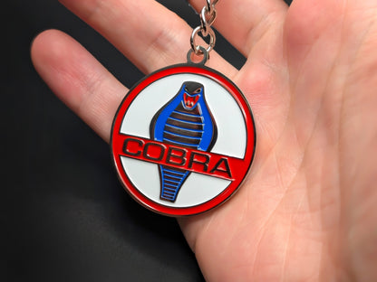Hand holding a circular Shelby Cobra enamel badge keychain to demonstrate the metallic weight and vibrant 3D finish.