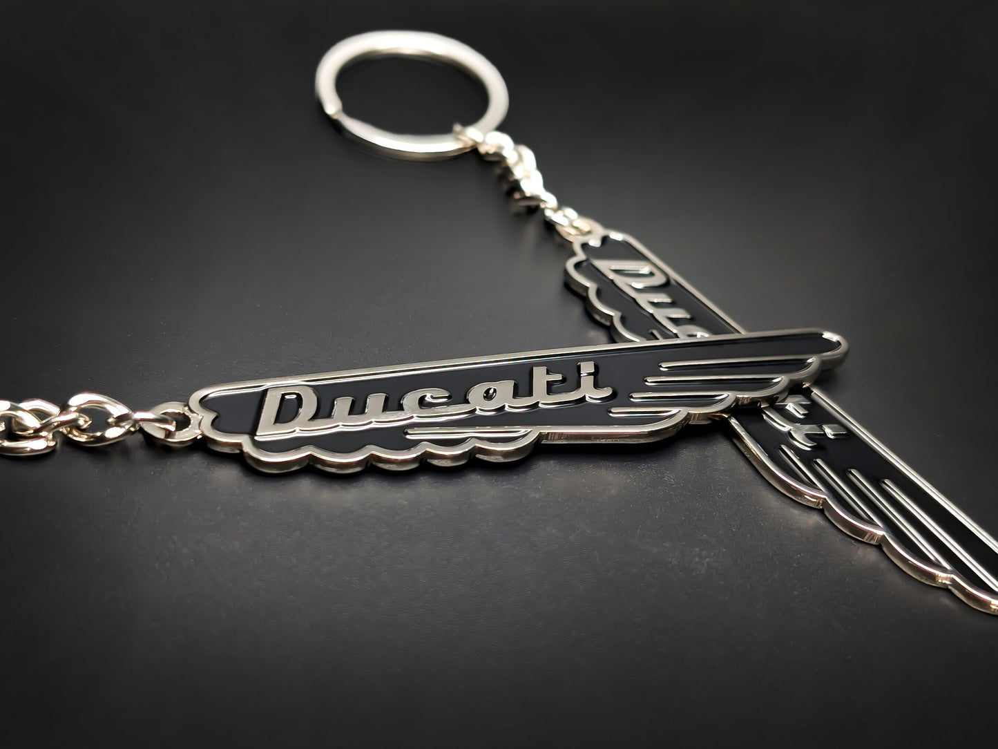 Two midnight black Ducati vintage script badge keychains with polished silver-tone wings on a dark surface.