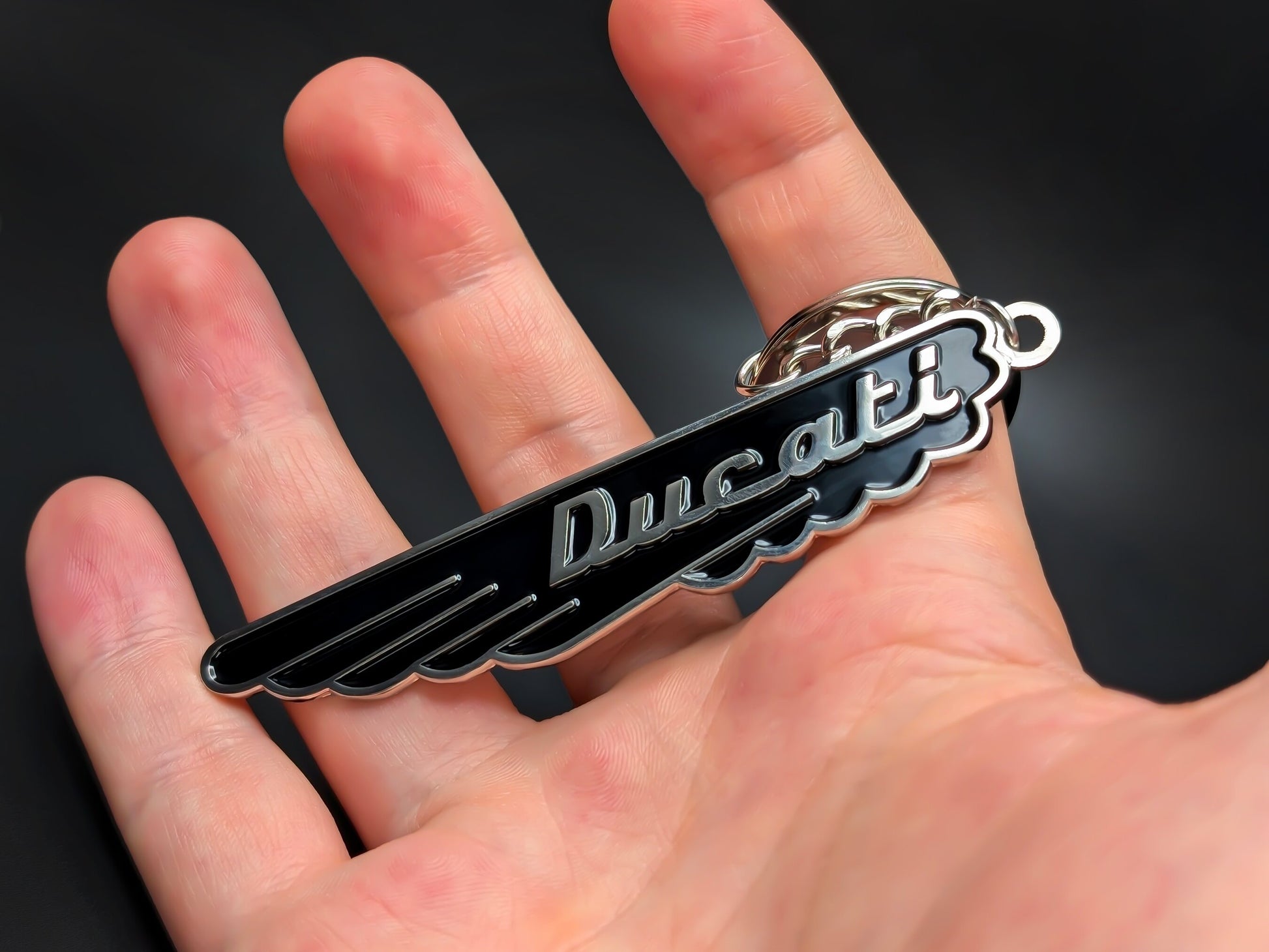 Hand holding the midnight black Ducati enamel keychain to demonstrate the premium metallic weight and detail.