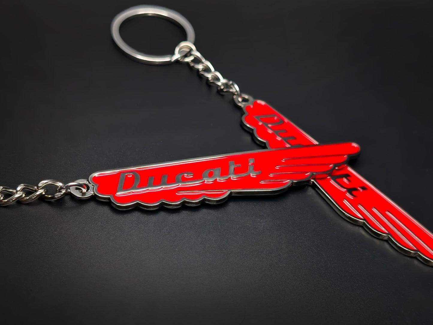 Close-up of two red Ducati vintage enamel keychains showcasing the vibrant color and 3D raised silver lettering.