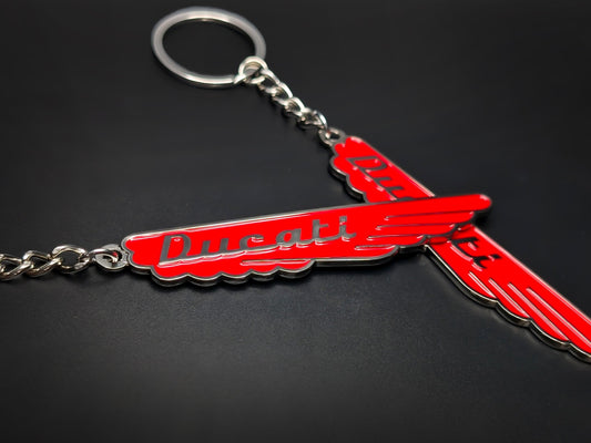 Close-up of two red Ducati vintage enamel keychains showcasing the vibrant color and 3D raised silver lettering.