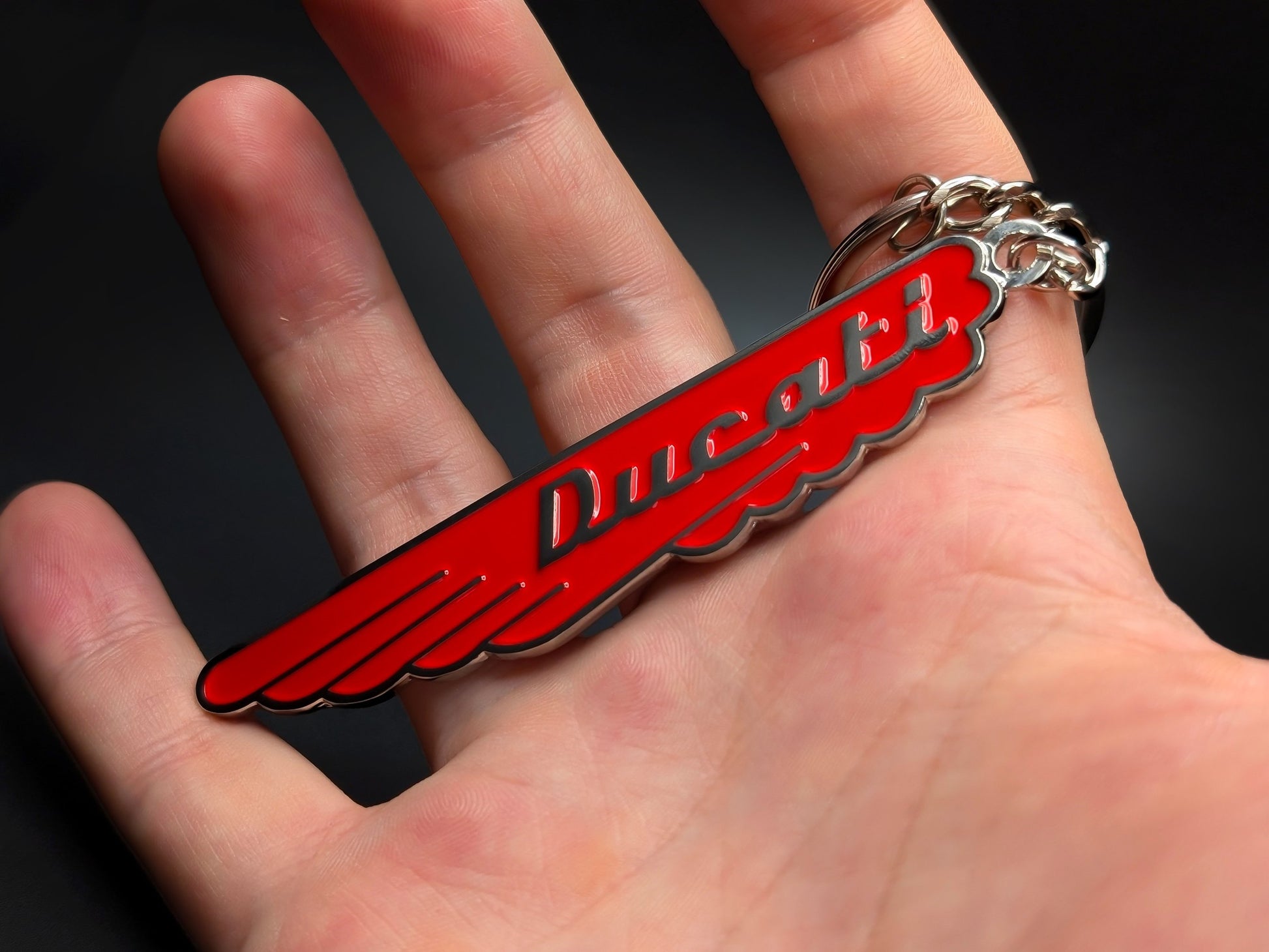 Hand holding the classic red Ducati enamel keychain highlighting the vibrant gloss finish and sturdy linked chain.