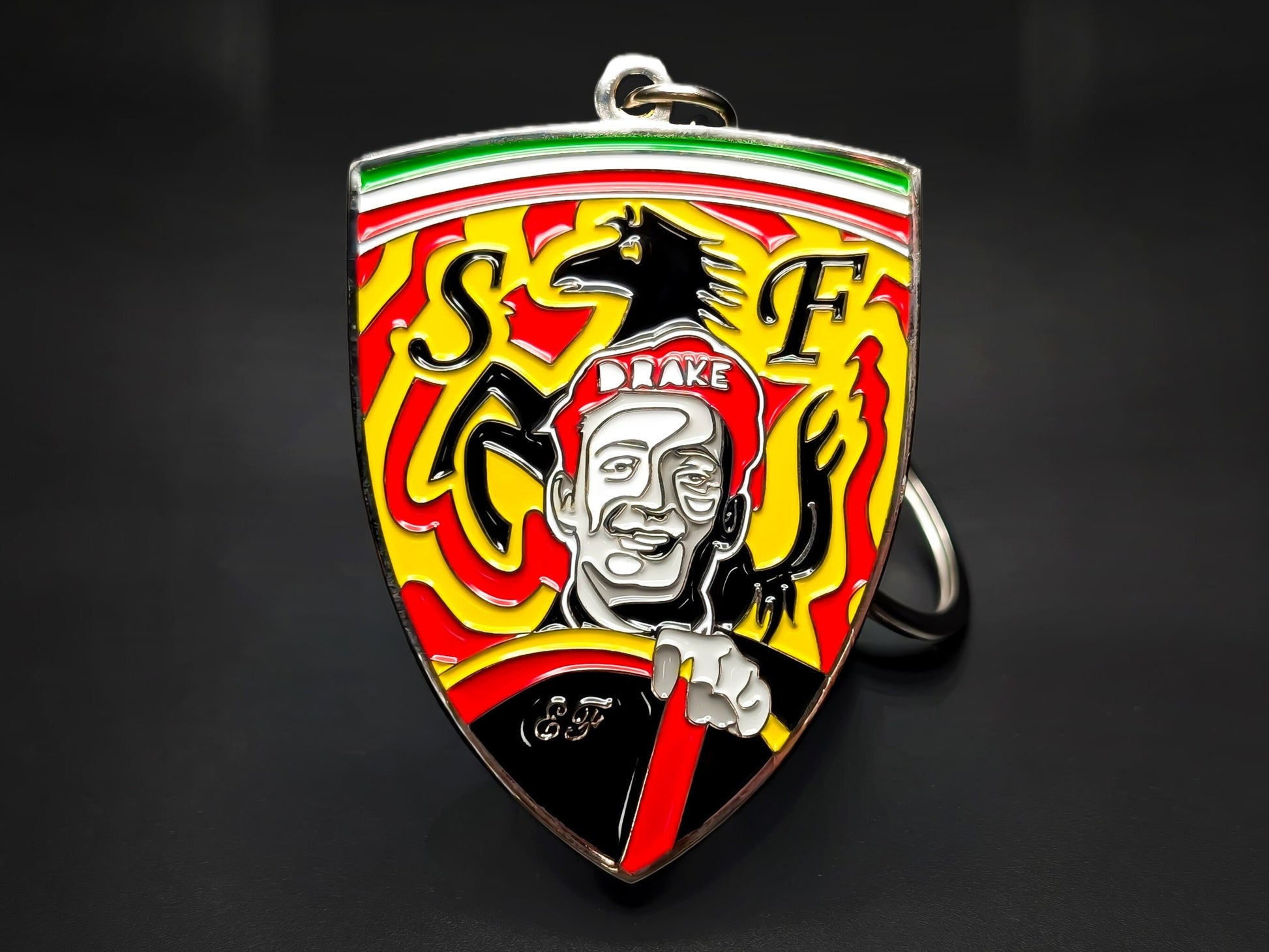 Vintage Enzo Ferrari badge keychain with "Drake" cap portrait, Scuderia Ferrari SF shield, and Prancing Horse logo on yellow enamel.