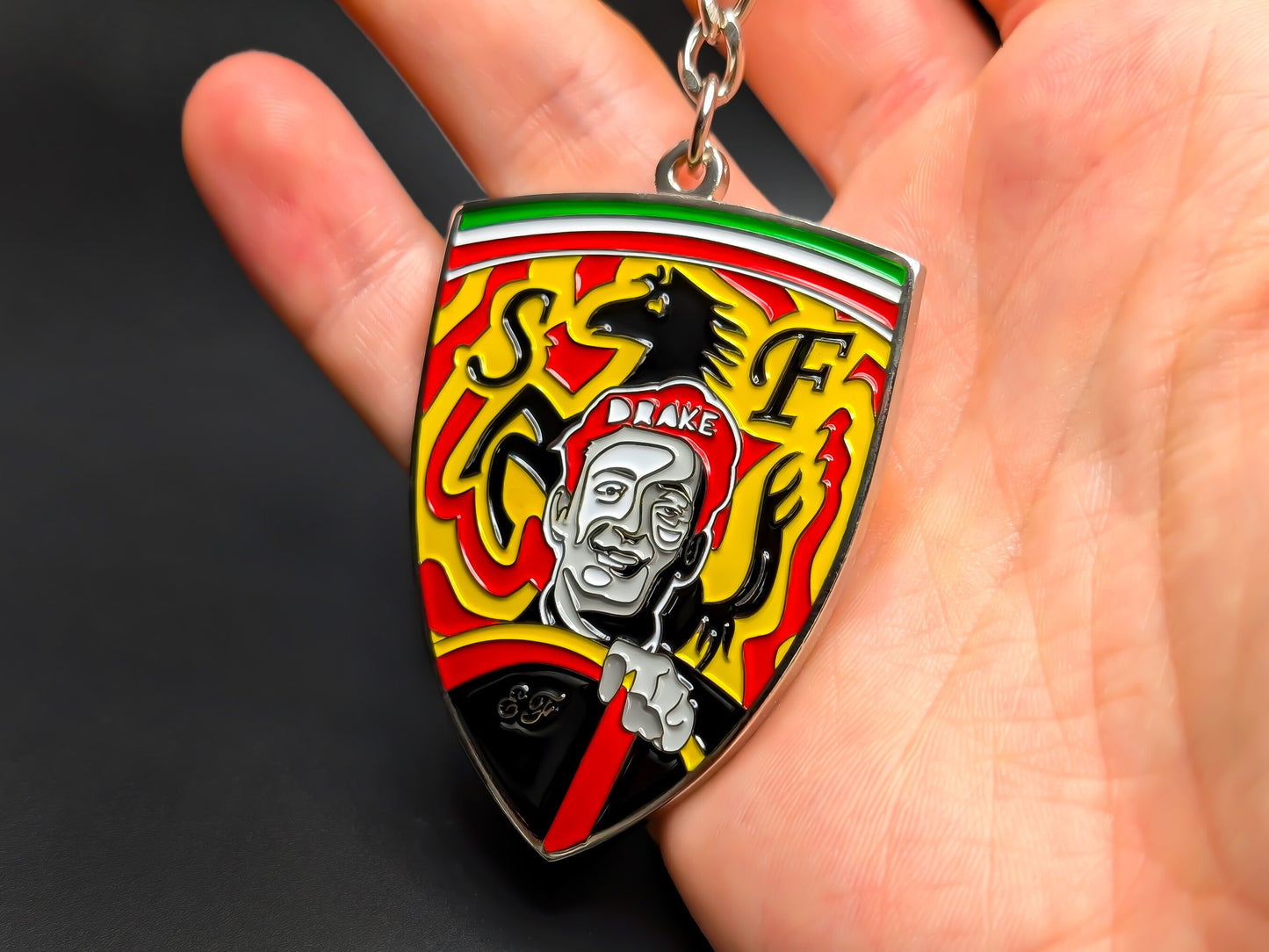 Hand holding a 3D Enzo Ferrari enamel badge keychain to demonstrate the premium metallic weight and vibrant yellow racing colors.