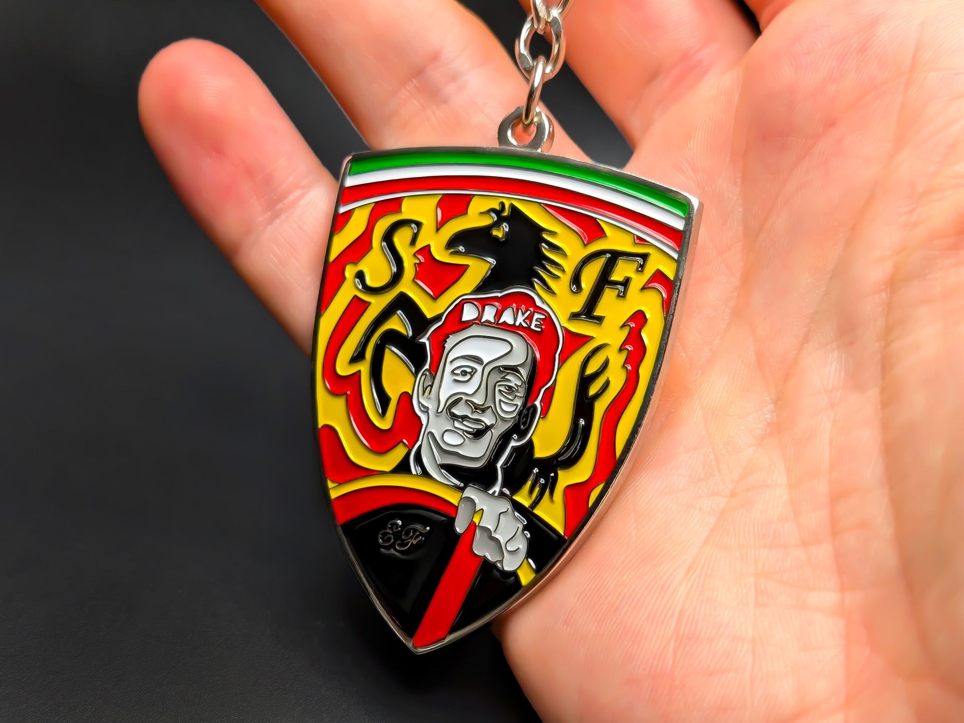 Hand holding a 3D Enzo Ferrari enamel badge keychain to demonstrate the premium metallic weight and vibrant yellow racing colors.