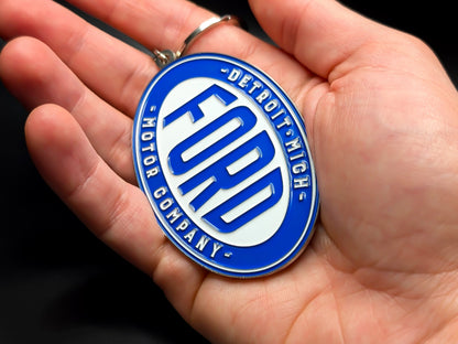 Hand holding an oval Ford Motor Company heritage keychain to demonstrate the premium metallic weight and vibrant color finish.