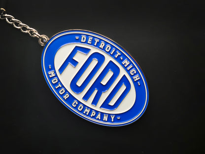 Close-up of a vintage Ford enamel keychain on a black surface, highlighting the 3D raised silver lettering and polished rim.