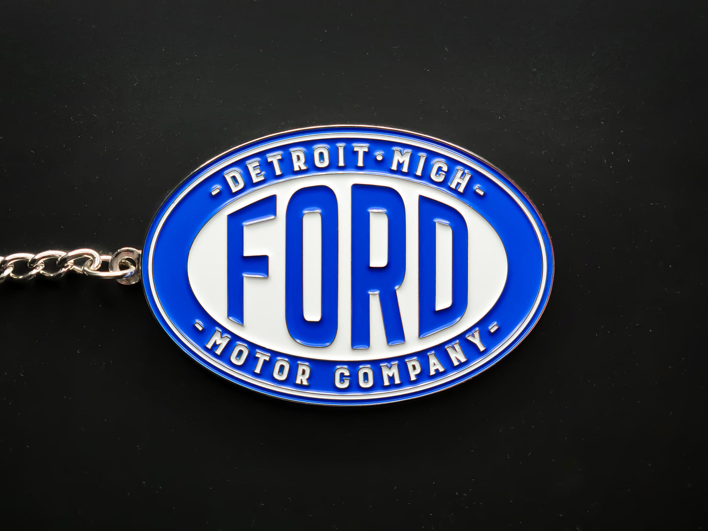 Overhead view of a Ford Detroit Motor Company keychain with a sturdy silver linked chain against a dark backdrop.