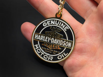 Hand holding a circular Harley-Davidson enamel badge keychain to demonstrate the premium metallic weight and detailed 3D gold finish.