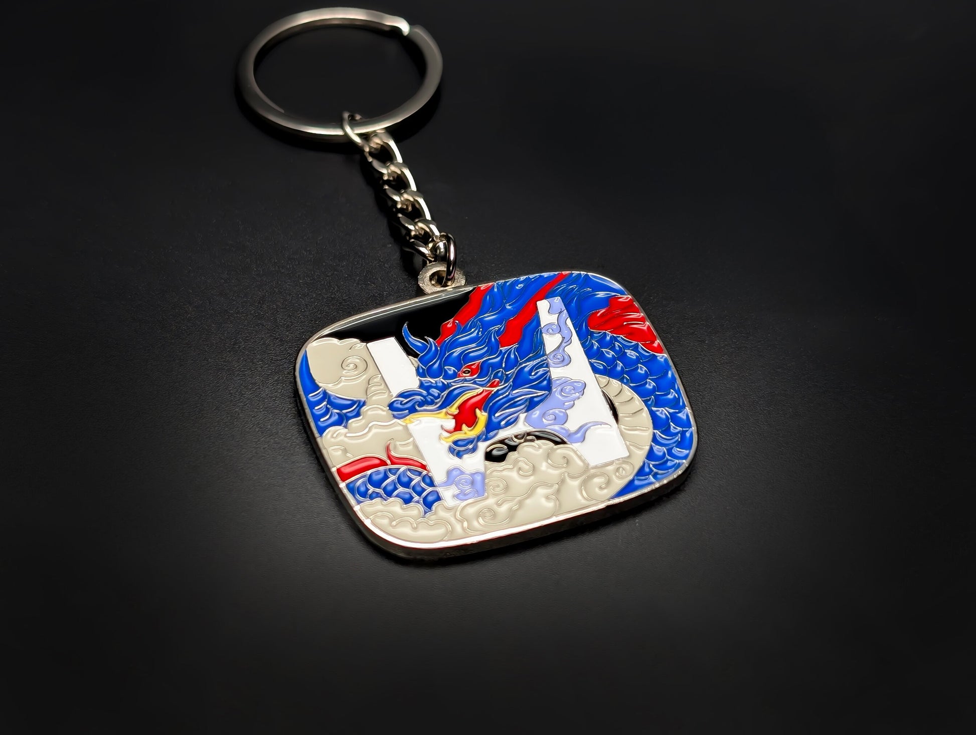 High-angle view of a Honda JDM badge keychain with a silver chain and ring against a dark background.