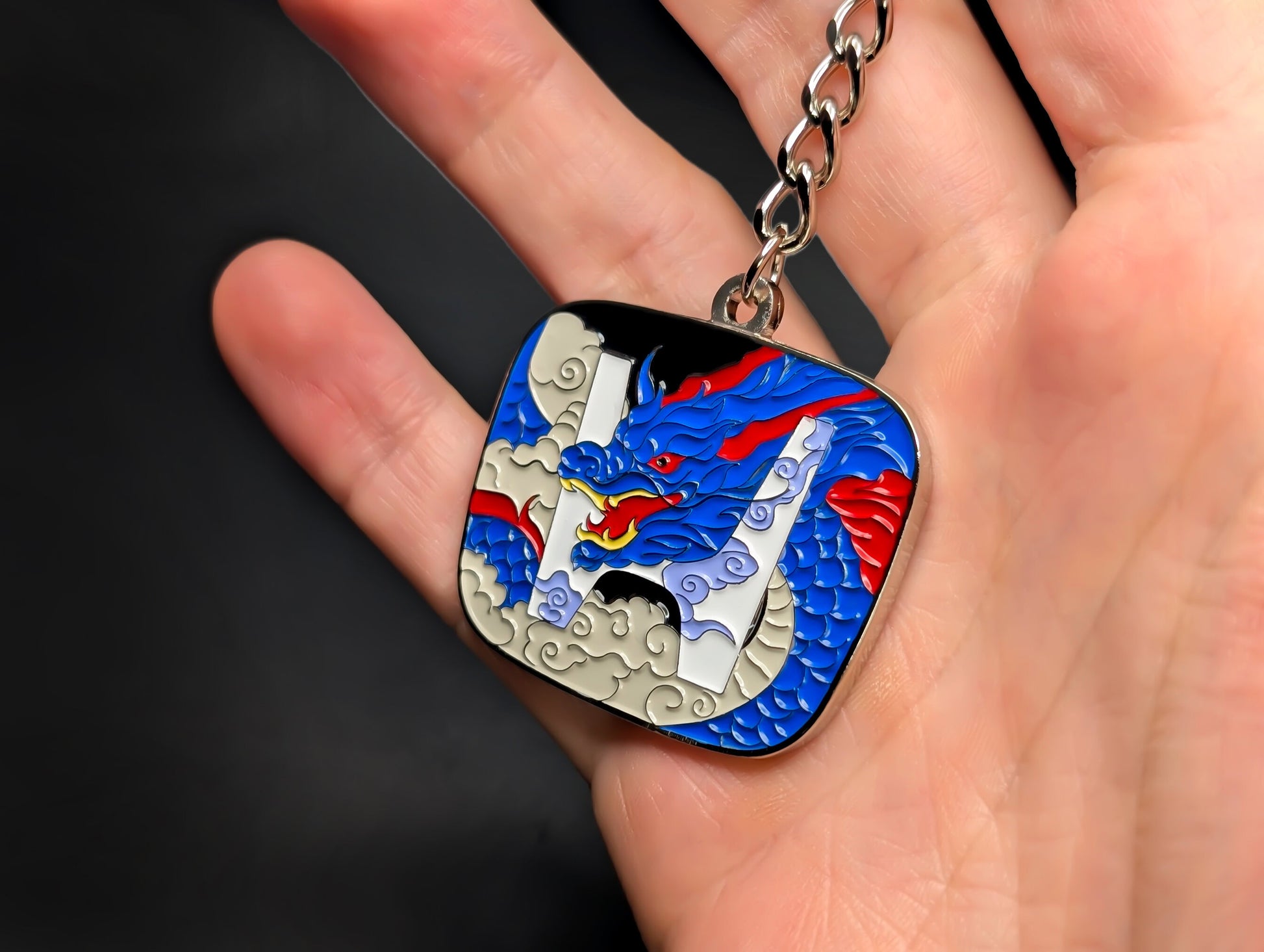A hand holding the Honda JDM badge keychain, showing the scale and vibrant enamel colors of the dragon design.