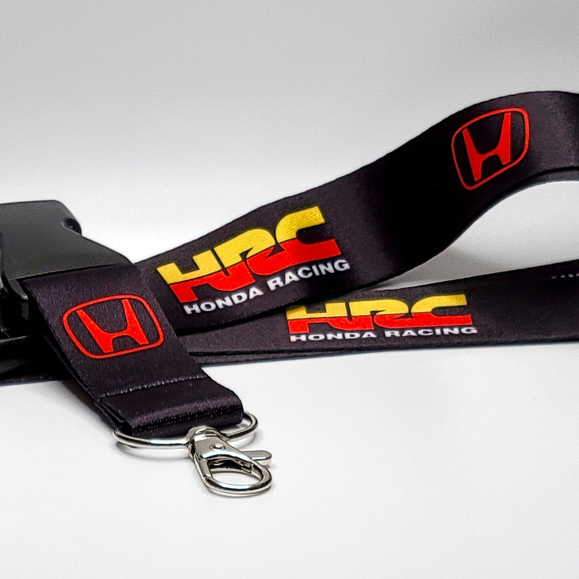 Black Honda lanyard with a red Honda H logo, a yellow-and-red HRC logo, and white Honda Racing text, coiled with a black breakaway clip and silver clasp on a light grey surface.
