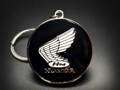 Vintage Honda motorcycle badge keychain featuring a white 3D wing logo and "HM" initials on a circular black enamel base.