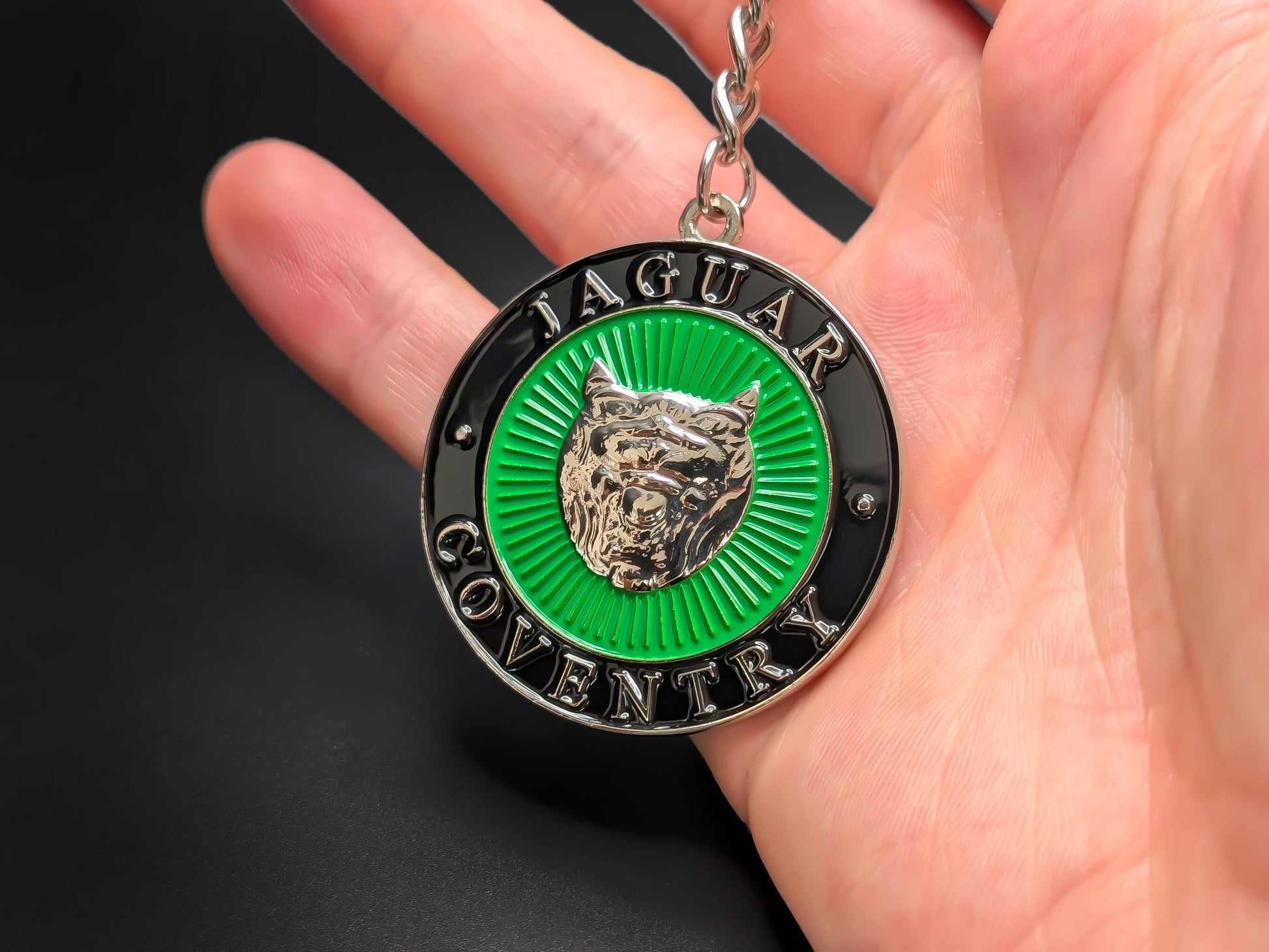 Hand holding a circular Jaguar Coventry enamel badge keychain to showcase the 3D raised Growler detail and premium metallic finish.