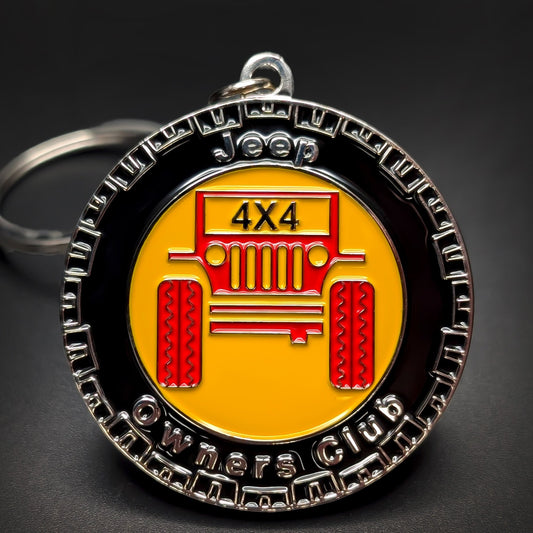Double-sided metal Jeep badge keychain with a tire-tread silver rim reading Jeep Owners Club, a red Jeep grille illustration marked 4X4 on yellow enamel, silver split ring, on a dark surface.