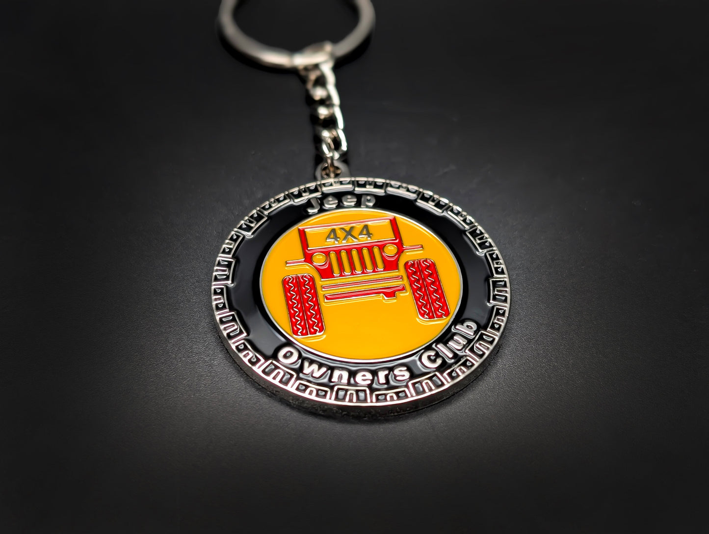 A Jeep Club badge keychain with a silver chain and ring, presented on a smooth, dark surface.
