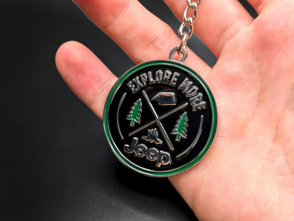 Hand holding a circular Jeep Explore enamel badge keychain to demonstrate the premium metallic weight and vibrant outdoor-themed details.