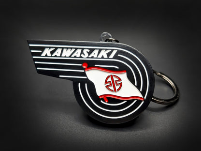 Vintage Kawasaki badge keychain featuring the winged wordmark and white River Mark flag with red accents on black enamel.