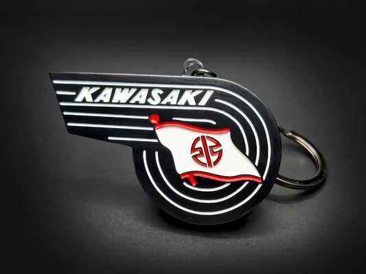 Vintage Kawasaki badge keychain featuring the winged wordmark and white River Mark flag with red accents on black enamel.