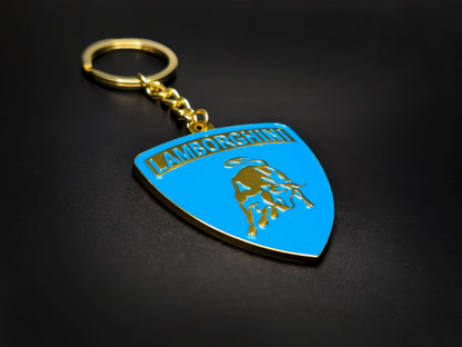 High-gloss blue Lamborghini badge keychain on a dark background, showcasing the polished gold-tone metal and chain.