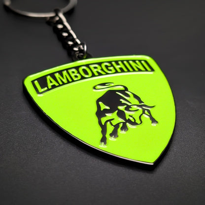Double-sided metal Lamborghini badge keychain in lime green enamel with black LAMBORGHINI lettering and a black bull emblem, attached to a split ring by a chain, on a dark textured surface.