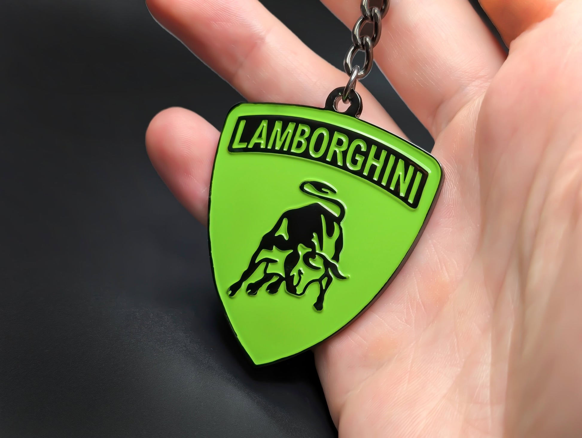 Hand holding a lime green and gunmetal Lamborghini enamel badge keychain to show the premium weight and metallic finish.