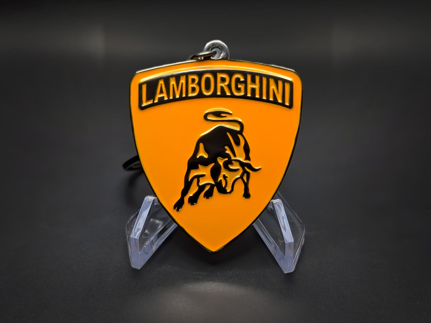 High-gloss orange Lamborghini badge keychain on a dark background, showing the polished black-tone metal rim.
