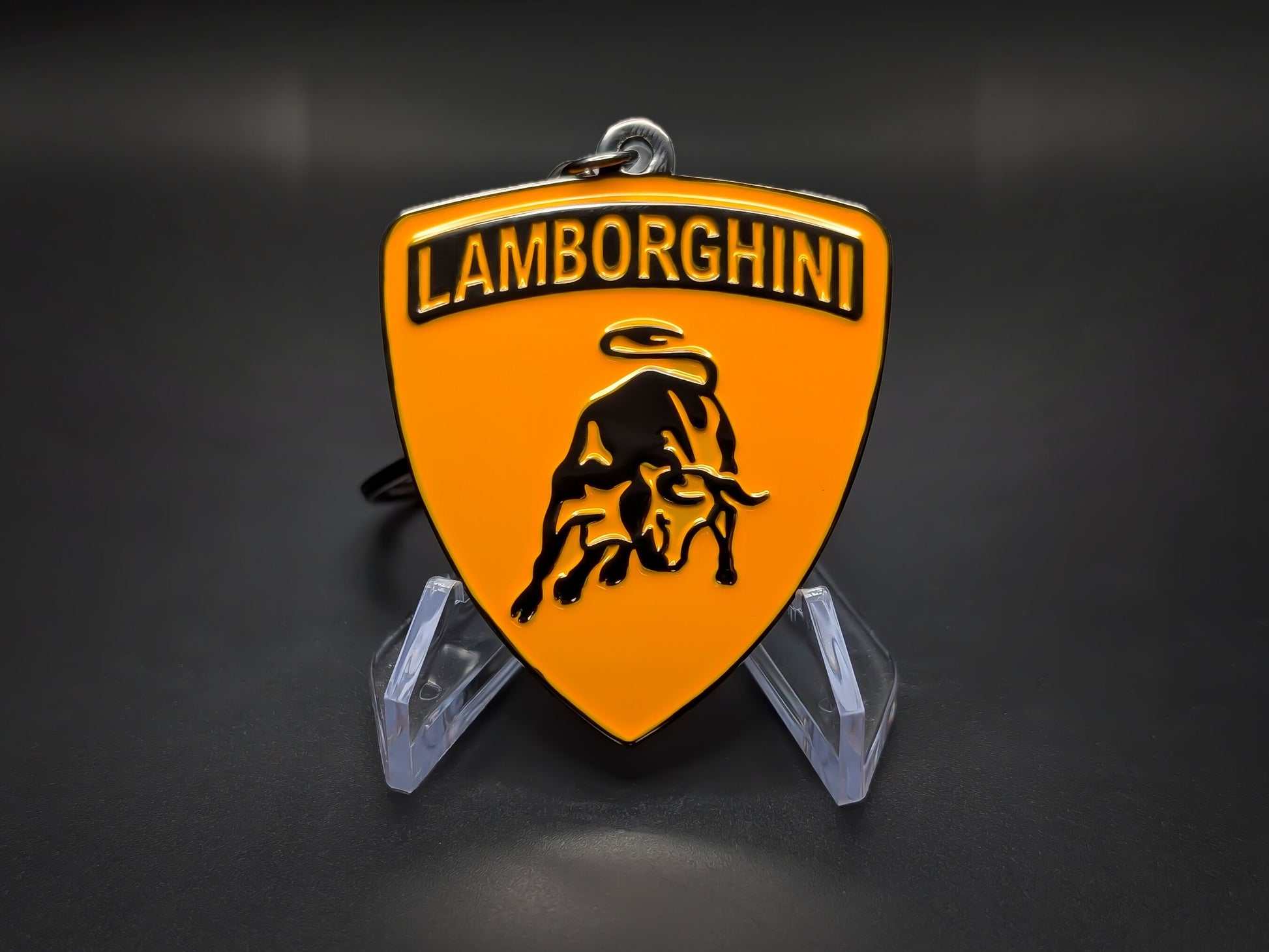 High-gloss orange Lamborghini badge keychain on a dark background, showing the polished black-tone metal rim.