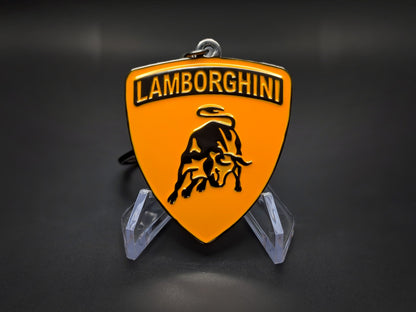 High-gloss orange Lamborghini badge keychain on a dark background, showing the polished black-tone metal rim.