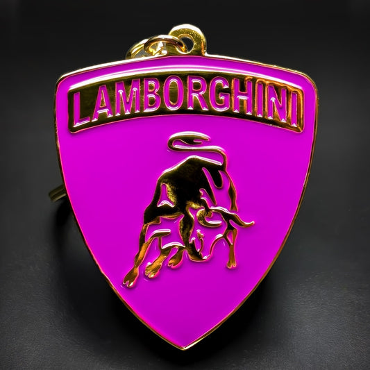 Double-sided metal Lamborghini badge keychain in magenta enamel with gold trim, magenta LAMBORGHINI lettering, and a gold bull emblem, hanging from a gold split ring on a dark surface.