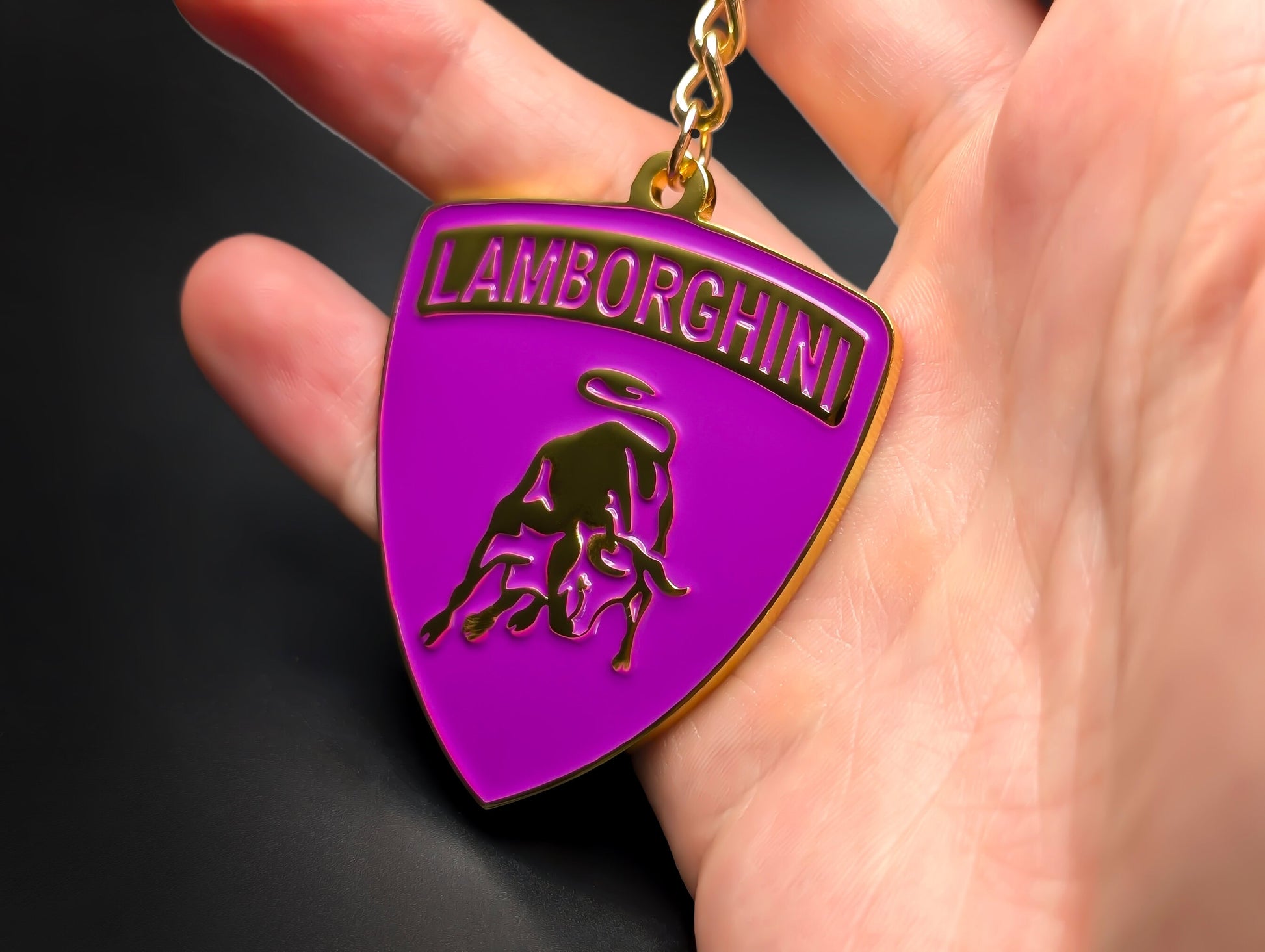 Hand holding a purple and gold Lamborghini enamel badge keychain to demonstrate the metallic weight and premium finish.