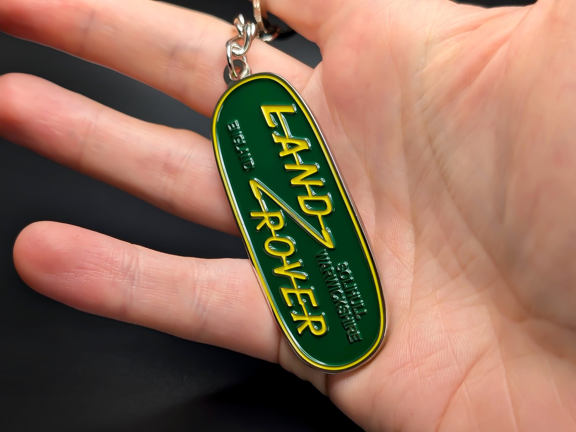 Classic Land Rover oval badge keychain held in hand, displaying the raised lettering and premium metallic finish.