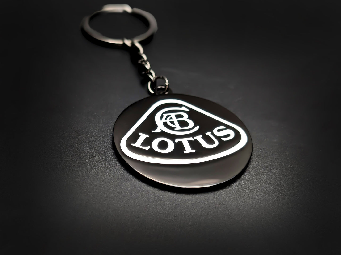 High-gloss black Lotus badge keychain on a dark background, showing the polished silver-tone chain and circular metal base.
