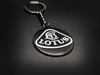 High-gloss black Lotus badge keychain on a dark background, showing the polished silver-tone chain and circular metal base.