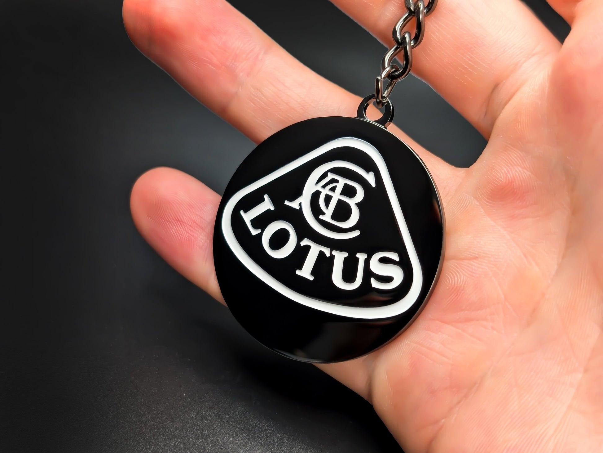 Hand holding a circular Lotus enamel badge keychain to demonstrate the high-contrast design and premium metallic finish.